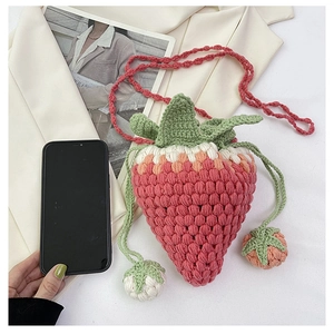 Detail of pink crochet strawberry bag with green leaf top beside a phone for scale