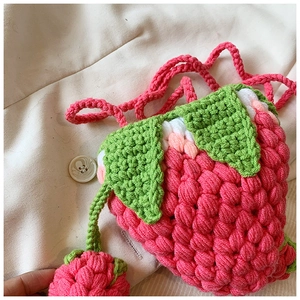 Detail of pink hand-crocheted strawberry bag with green leaf accents and matching strap