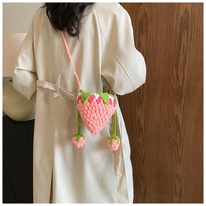 Close-up of a handmade pink crochet strawberry crossbody bag with green leaf detail