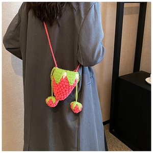 Detail of pink hand-knitted strawberry crossbody bag with green leaf top and mini charms