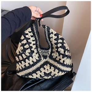 Detail of hand-woven straw tote with black hollow pattern and leather shoulder strap