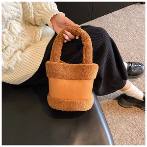 Detail of plush brown lamb wool bucket bag with leather splicing held by a model