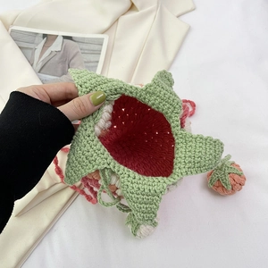 Handmade crochet strawberry crossbody bag in red and green yarn on silk background