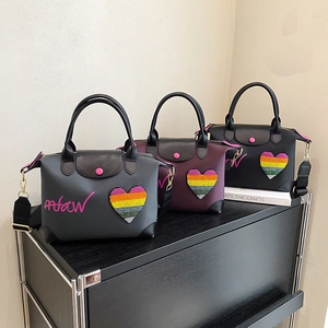 Three nylon tote bags with heart sequins in black, purple, and grey on a black shelf