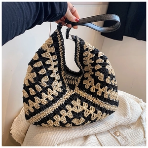 Detail of hand-woven straw bucket bag showing black geometric hollow knit patterns