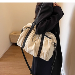 Detail of white nylon tote bag showing side drawstring and black adjustable strap