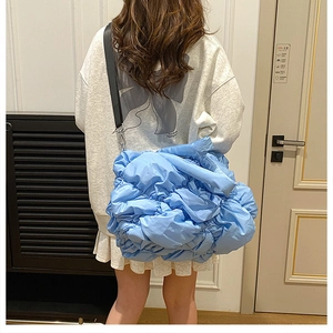 Gros plan du sac matelassé bleu clair avec sa bandoulière noire large et réglable