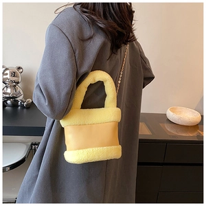 Detail of yellow plush bucket bag with leather patchwork and gold chain strap on model