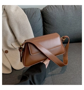Detailed view of brown PU leather square shoulder bag with gold hardware on a sofa