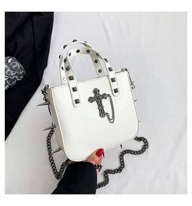 Close-up of gothic white handbag with silver cross, chain, and metallic spikes