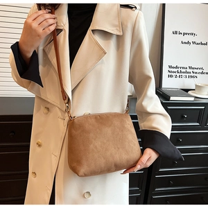 Detail of suede crossbody bag with gold zipper and adjustable strap worn on beige coat