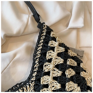 Detail view of woven straw tote bag with black and white contrast knit pattern and leather strap
