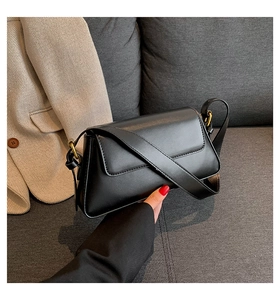 Close-up of black leather rectangular handbag with wide strap and gold metal hardware