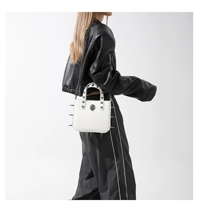 Close-up of white gothic bag with metal spikes and skull detail worn with leather jacket