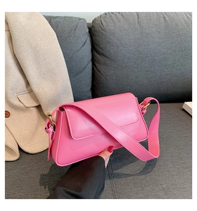 Detail of pink faux leather crossbody bag with flap cover and wide strap on grey background