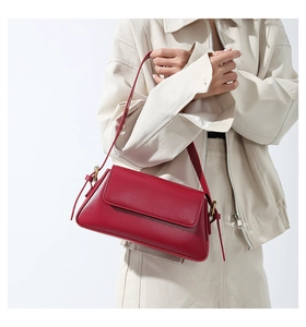 Detail of red leather shoulder bag with vintage gold buckle on beige blazer background