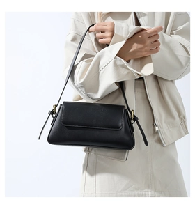 Detail view of black leather baguette bag with gold buckle and adjustable shoulder strap