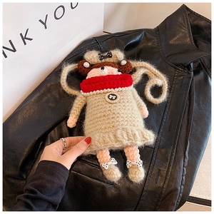 Détail du sac poupée au crochet fait main avec écharpe rouge et collier de perles sur cuir