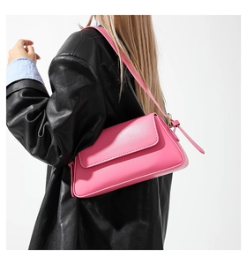 Close-up of bright pink leather baguette bag styled on a model with a black coat