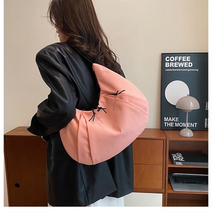 Detalle de bolso medialuna de nailon rosa con lazos en modelo con chaqueta de cuero negra