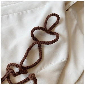 Détail macro d'une bandoulière tressée marron avec texture torsadée sur tissu tricoté blanc