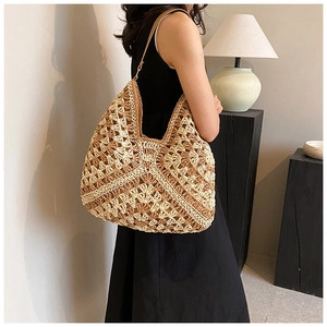 Close-up of large woven straw shoulder bag with contrast knit patterns and leather straps