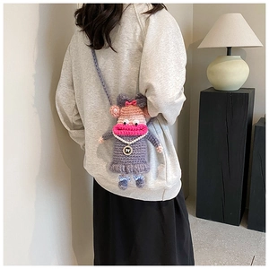 Détail du sac poupée au crochet violet avec nœud rose et collier de perles blanches
