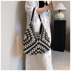 Close-up of contrast woven straw bag with black leather strap and floral pattern details