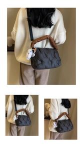 Detailed view of black quilted down bag with brown handle and plush rabbit pendant