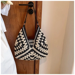 Detail of crochet straw shoulder bag featuring black and beige floral patterns with leather strap