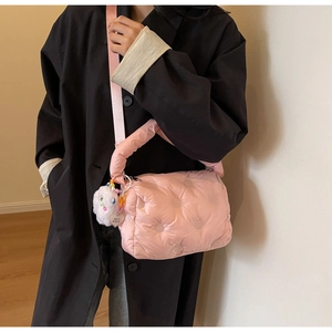 Detail of pink quilted puffer bag showing plush rabbit charm and heart tag on black coat