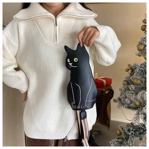 Cute black cat-shaped crossbody bag with a striped strap shown in a Christmas setting