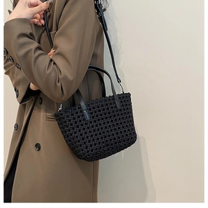 Detail of black woven bucket bag with leather handles and adjustable shoulder strap