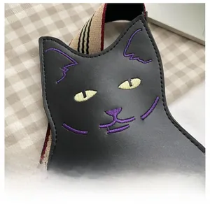 Detailed embroidery of purple cat whiskers and yellow eyes on a black leather handbag