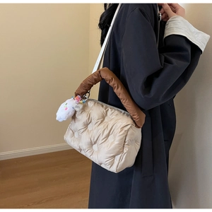 Close-up of quilted cream puffy bag with brown handles and a plush cloud charm