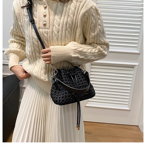 Detail of black woven bucket bag with leather handle and drawstring on beige knit sweater