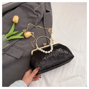 Detail of black sequin evening bag with pearl handle and gold clasp on white fabric