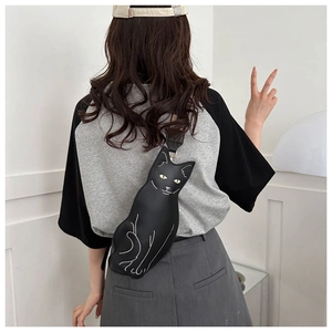 Close-up of black cat-shaped crossbody bag with yellow eyes and white stitching detail
