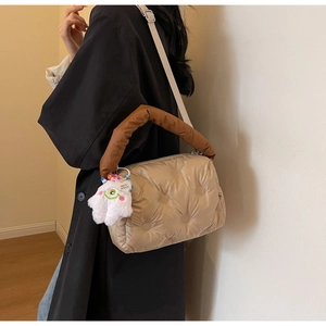 Close-up of beige quilted puffer bag featuring a plush monster charm and padded handle