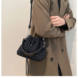 Detail of black woven bucket bag showing drawstring closure and leather straps on model