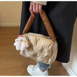 Close-up of champagne quilted puffer bag with brown satin handles and plush monster charm
