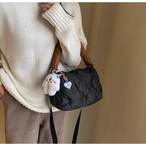 Detail of black quilted puffer bag with brown handles and a heart charm on side