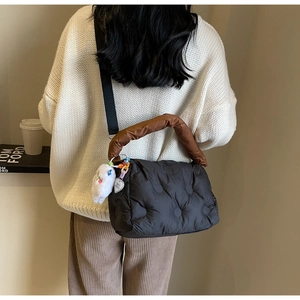 Detail of a puffy quilted down crossbody bag with a plush charm on a fashion model