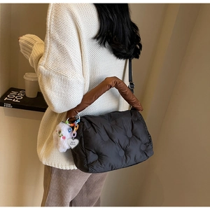 Detail of quilted puffer bag with brown handles and a cute plush monster charm accessory