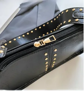 Detail of smooth gold zipper and metallic studs on black faux leather handbag