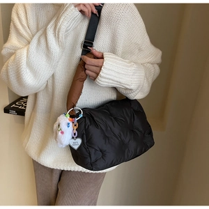 Close-up of black quilted down handbag with plush heart charm and adjustable wide strap
