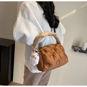 Close-up of brown quilted puffer bag with beige padded handle and plush bear charm