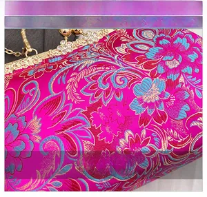Close-up of pink silk evening bag with blue floral embroidery and gold rhinestone clasp