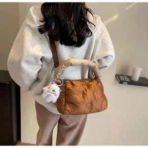 Detailed view of brown quilted down bag with beige fluffy handle and plush monster charm