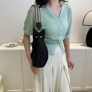 Cute black cat shaped crossbody bag with striped strap worn by a model in casual outfit